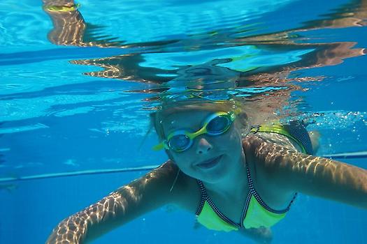 Flicka med simglasögon simmar i pool