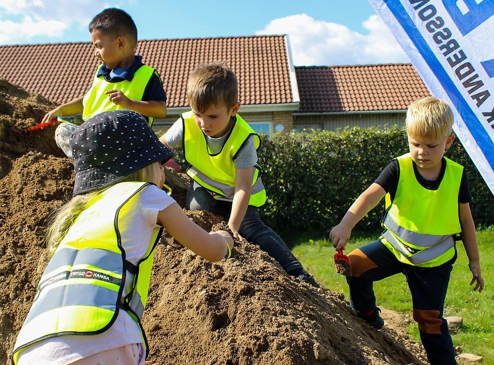 Fyra förskolebarn gräver med spadar i en grushög. 