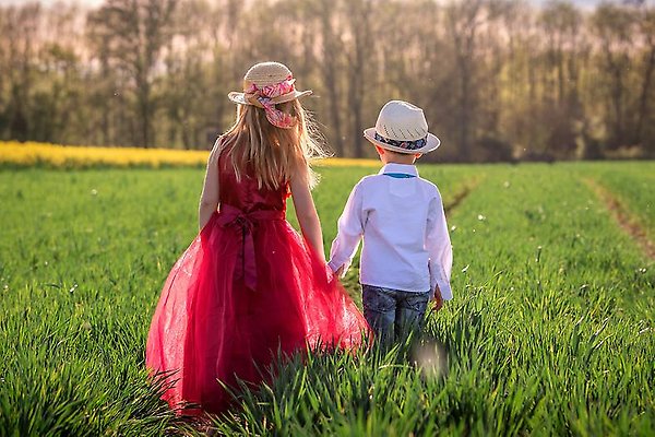 Bild på pojke och flicka som håller handen ute på ett vackert gräsfält.